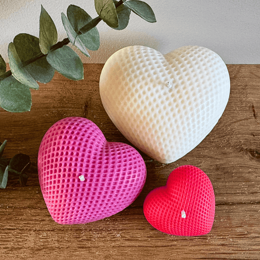 Drie hartjes kaarsen in verschillende maten: crème, donker roze en rood.